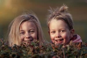 two happy kids looking over a bush